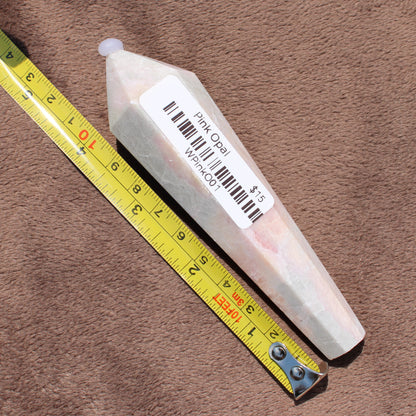 Pink Opal Wand crystal from Different Branches LLC next to measuring tape on brown surface