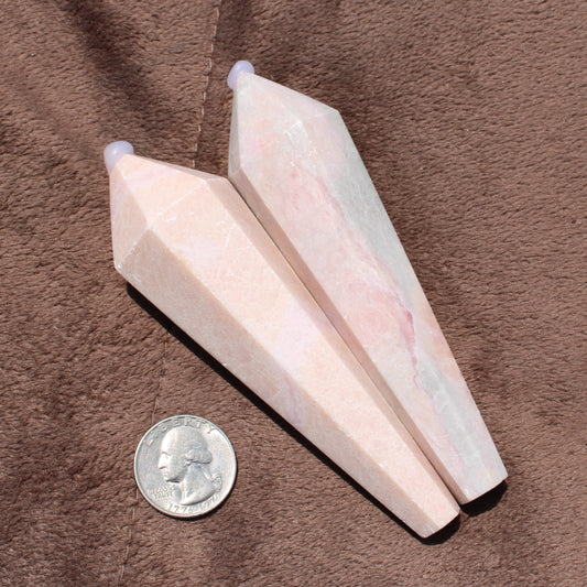 Two polished Pink Opal Wand crystals next to a quarter for size comparison on brown fabric