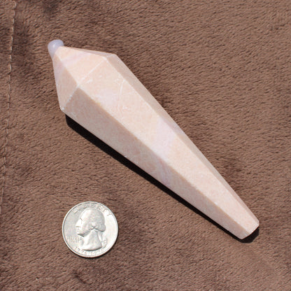 Faceted Pink Opal Wand crystal displayed next to a quarter for size reference on a brown fabric