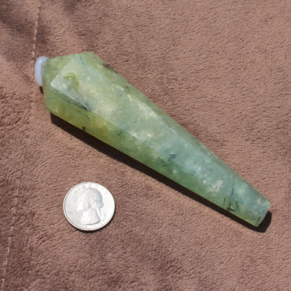 Green polished Prehnite Wand crystal next to a quarter for size comparison on brown fabric