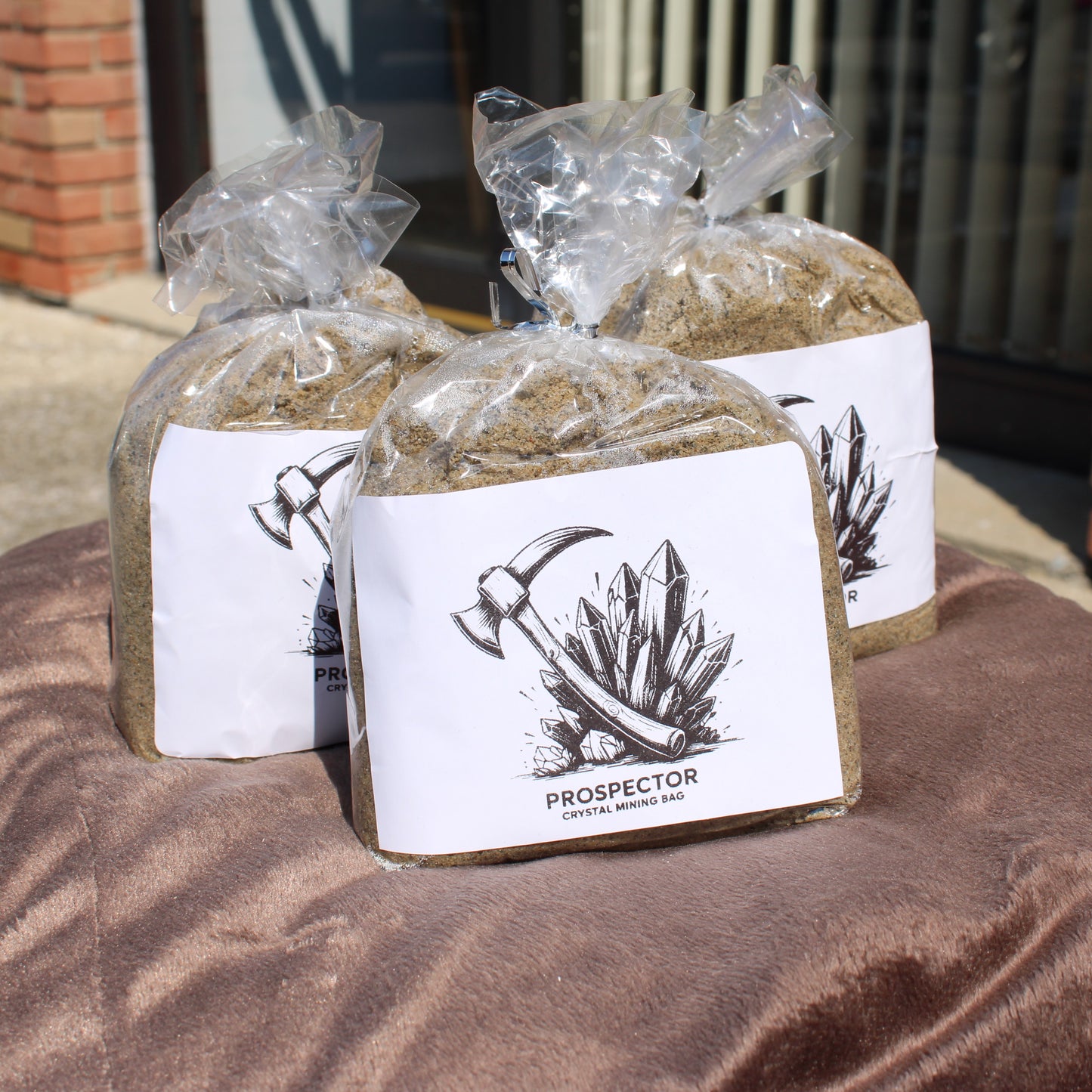 Three Prospector crystal mining sand bags with pickaxe illustration on labels displayed outdoors Gem mining mystery bags