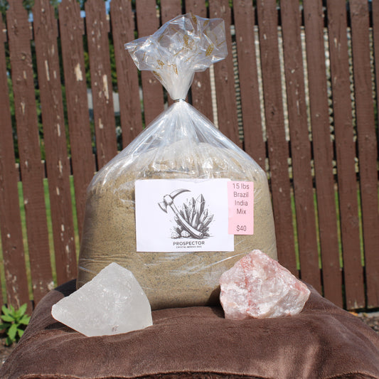 Clear plastic 15 lb large gem mining mystery bag with two rough clear and pink crystals on cloth