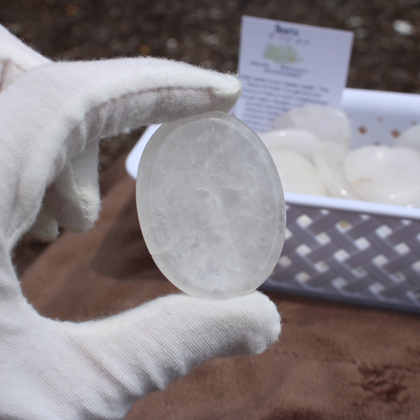 Gloved hand holding a clear Quartz Worry Stone with a basket of similar stones in the background