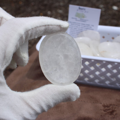 Gloved hand holding a clear Quartz Worry Stone with a basket of similar stones in the background