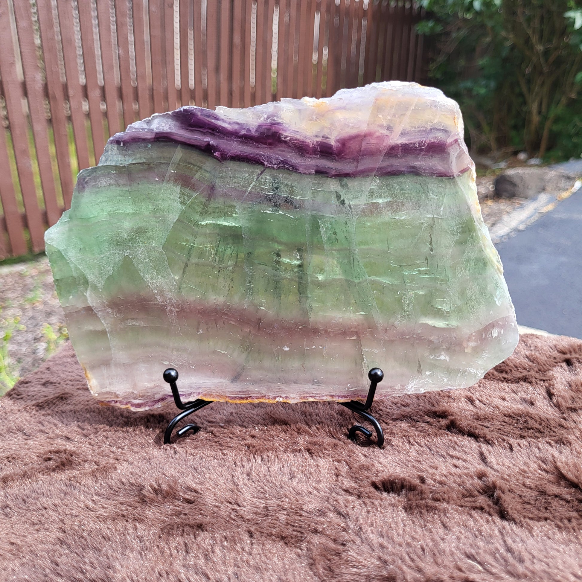 Rainbow Flourite Slab showcasing vibrant purple and green hues, displayed on a black stand.