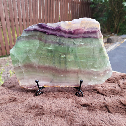 Rainbow Flourite Slab showcasing vibrant purple and green hues, displayed on a black stand.