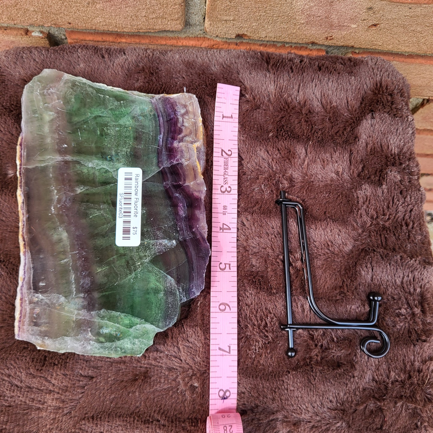 Rainbow Fluorite Slab on a soft surface with a measuring tape for size reference and a metal display stand