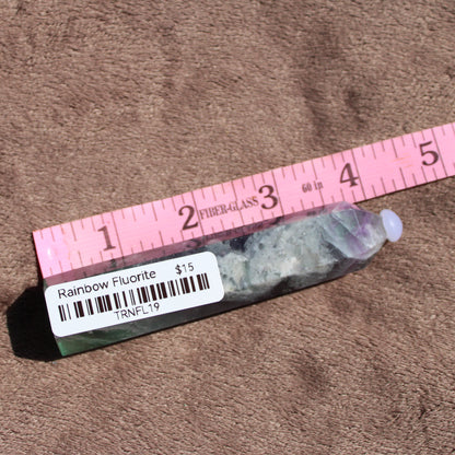 Rainbow Fluorite tower with vibrant colors and unique natural patterns displayed on a sandy background