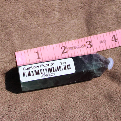 Rainbow Fluorite tower displayed on a textured surface with a ruler for size reference