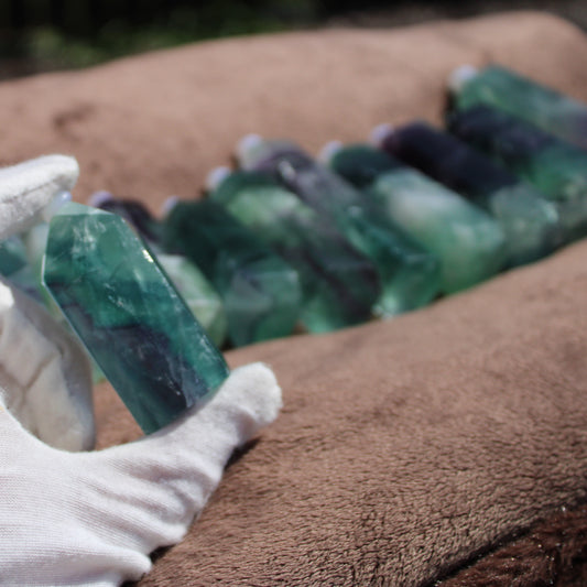 Hand holding a Rainbow Fluorite tower among a row of colorful translucent crystals