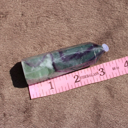 Rainbow Fluorite tower with smooth surface and vibrant green and purple colors on a soft background