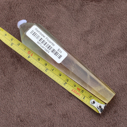 Rainbow Fluorite Wand crystal with label and yellow measuring tape on brown fabric background
