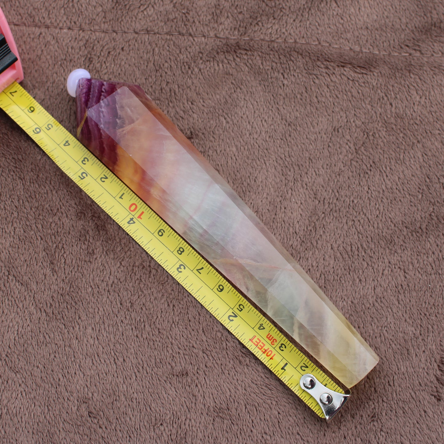 Rainbow Fluorite Wand crystal with multicolor bands placed next to measuring tape on brown fabric