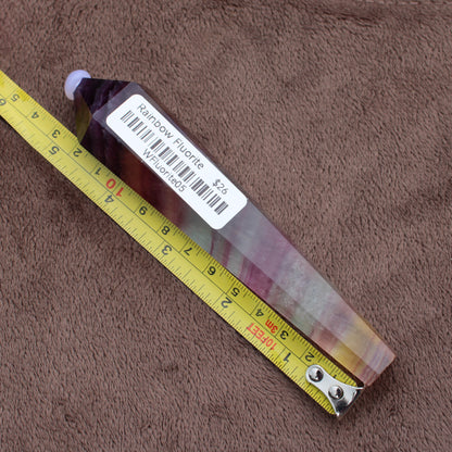 Rainbow Fluorite Wand crystal lying next to a yellow measuring tape on a brown fabric background