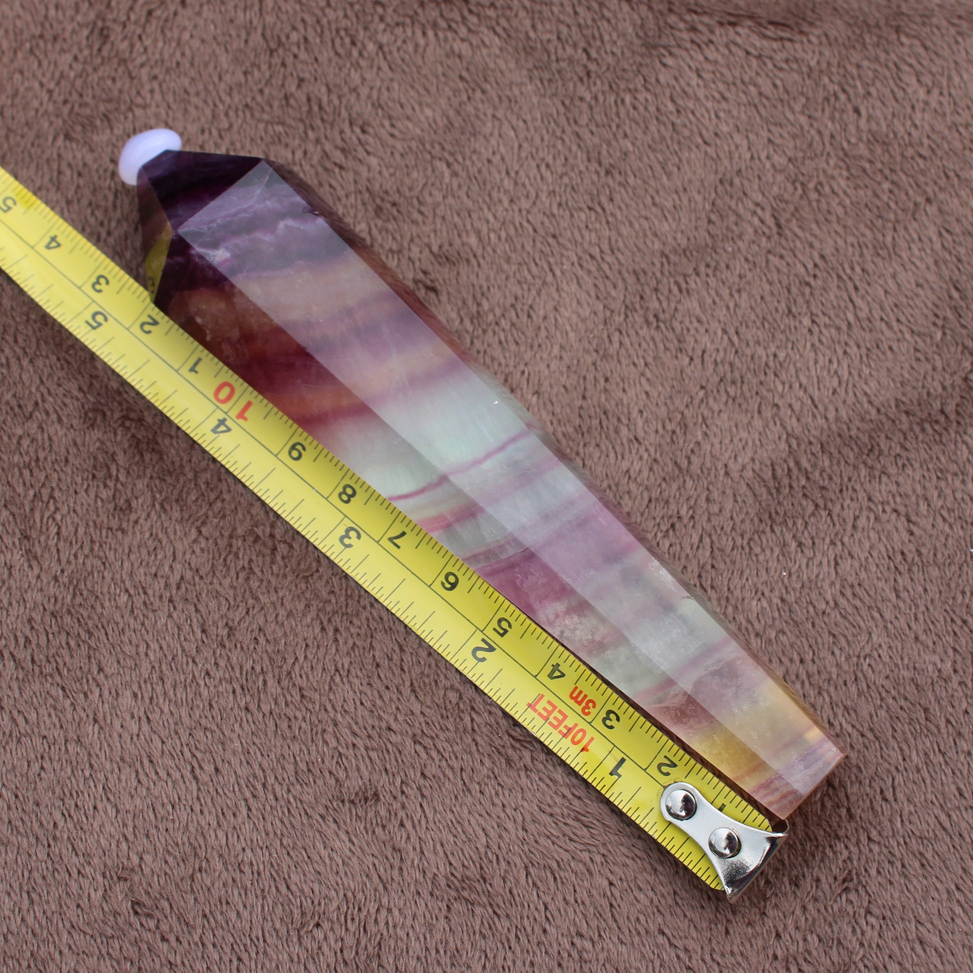 Rainbow Fluorite Wand crystal measuring about 10 inches on a brown textured surface