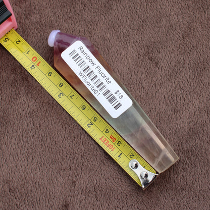 Rainbow Fluorite Wand crystal placed next to a measuring tape on a brown fabric background