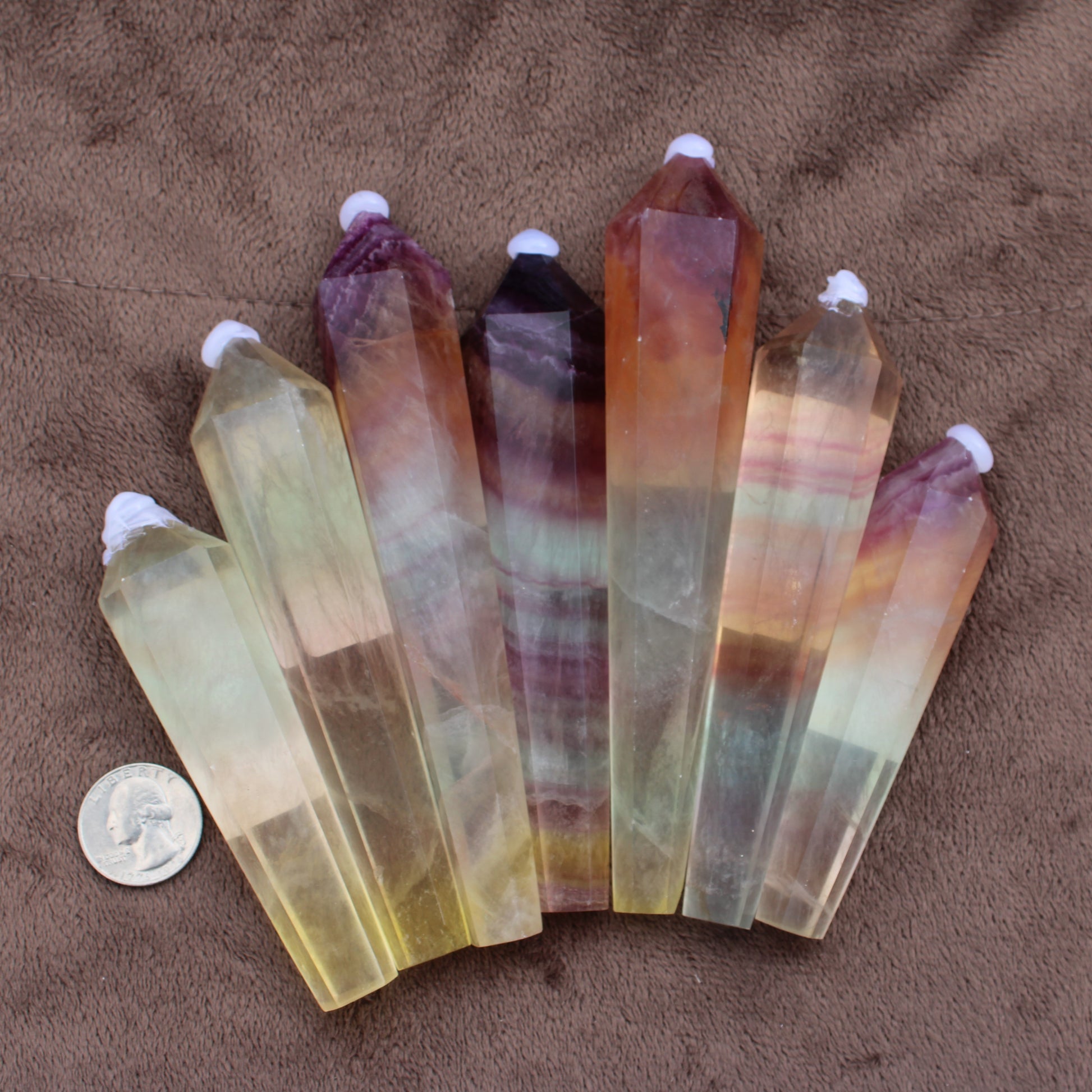 Rainbow Fluorite Wand crystal points in various colors arranged with a quarter for size comparison