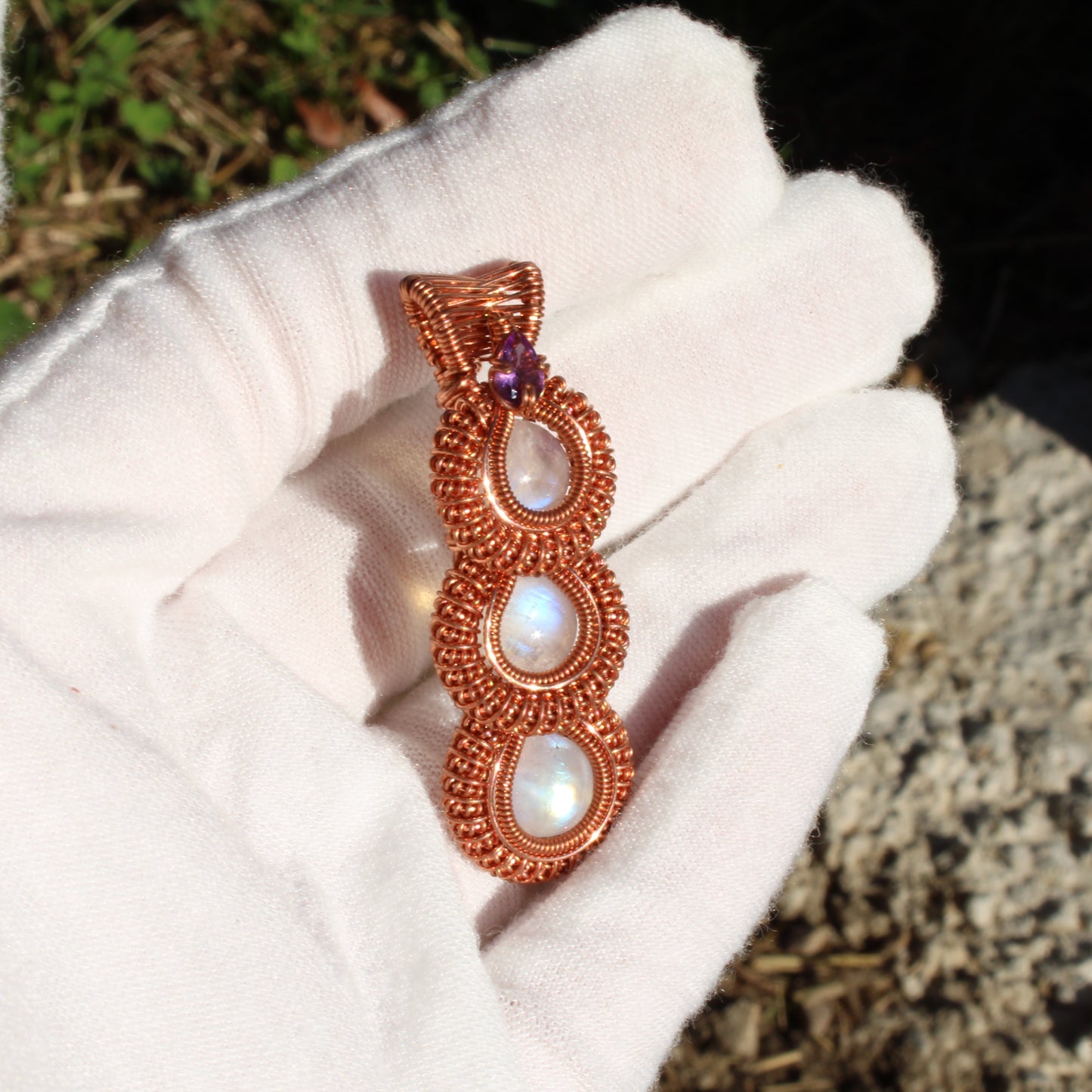 Rainbow moonstone copper pendant with intricate wire wrapping and a purple accent stone