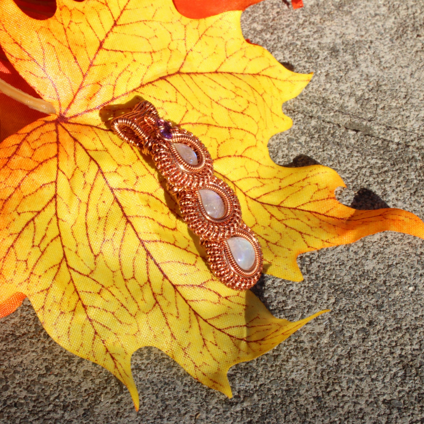 Rainbow moonstone copper pendant elegantly displayed on a vibrant autumn leaf