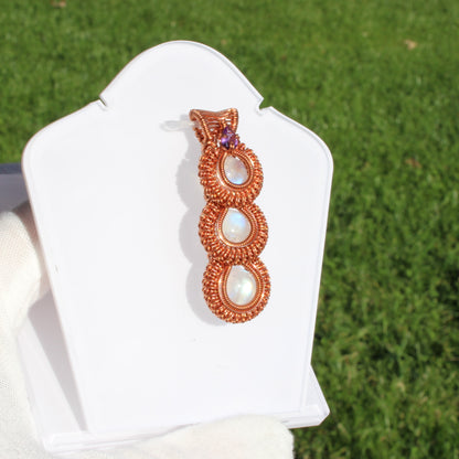 Rainbow moonstone copper pendant featuring three elegantly wrapped gemstones on a display stand