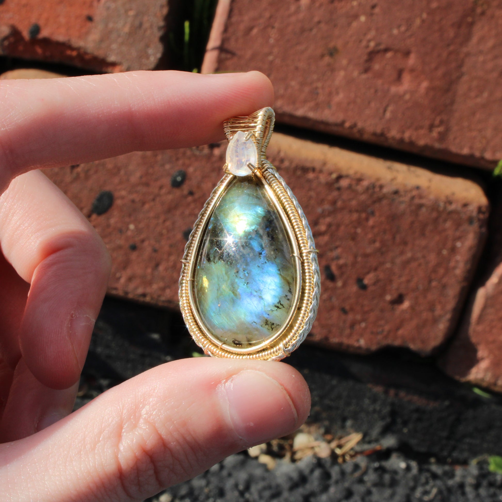 Rainbow Moonstone & Labradorite 14k Gold fill pendant held in hand against a brick background