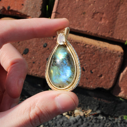 Rainbow Moonstone & Labradorite 14k Gold fill pendant held in hand against a brick background
