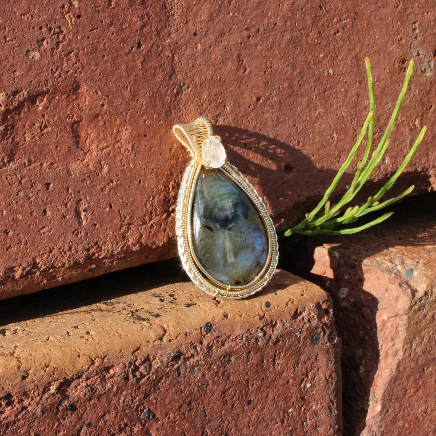 Rainbow Moonstone & Labradorite 14k Gold fill pendant resting on rustic brick with green plant decor