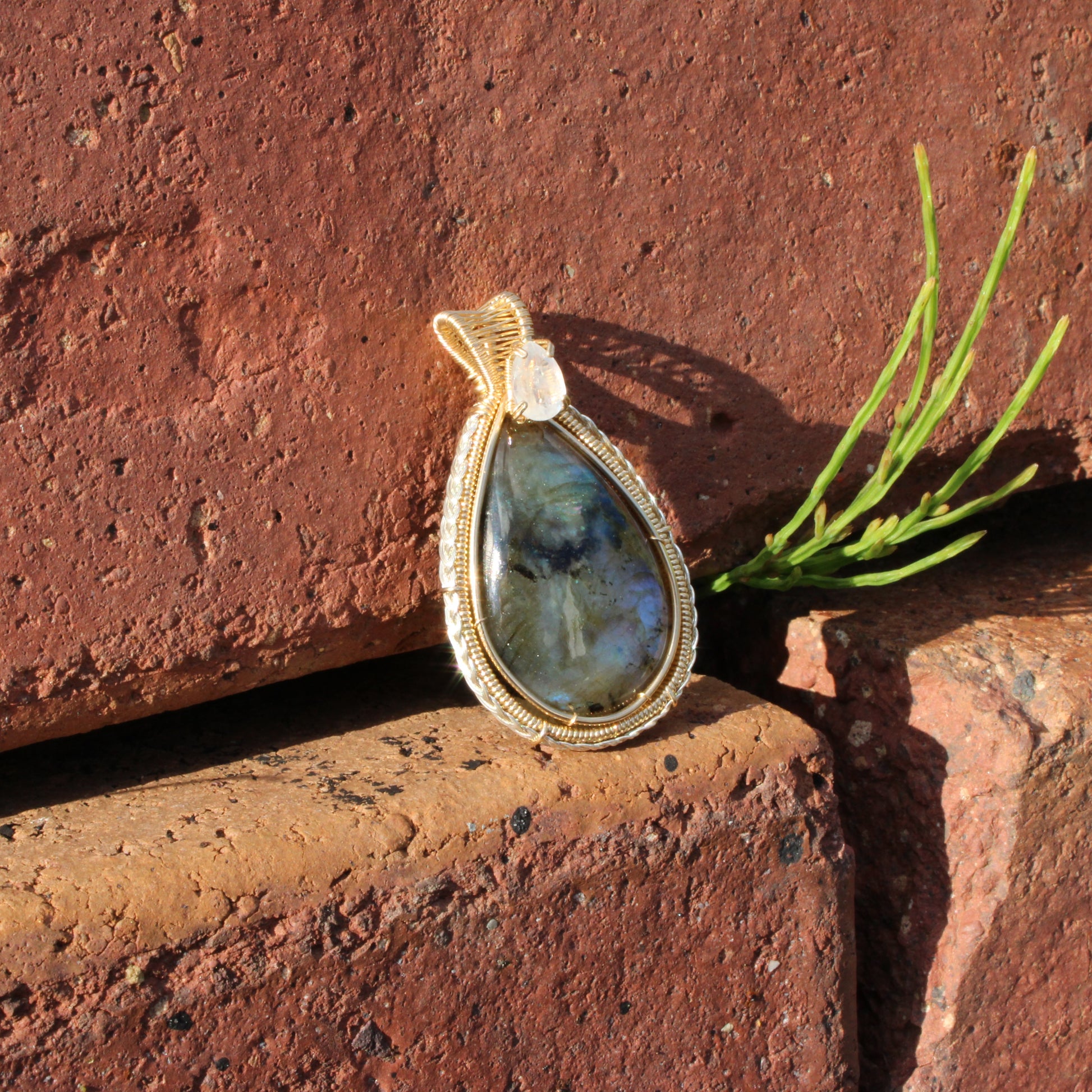 Rainbow Moonstone & Labradorite 14k Gold fill pendant resting on rustic brick with green plant decor