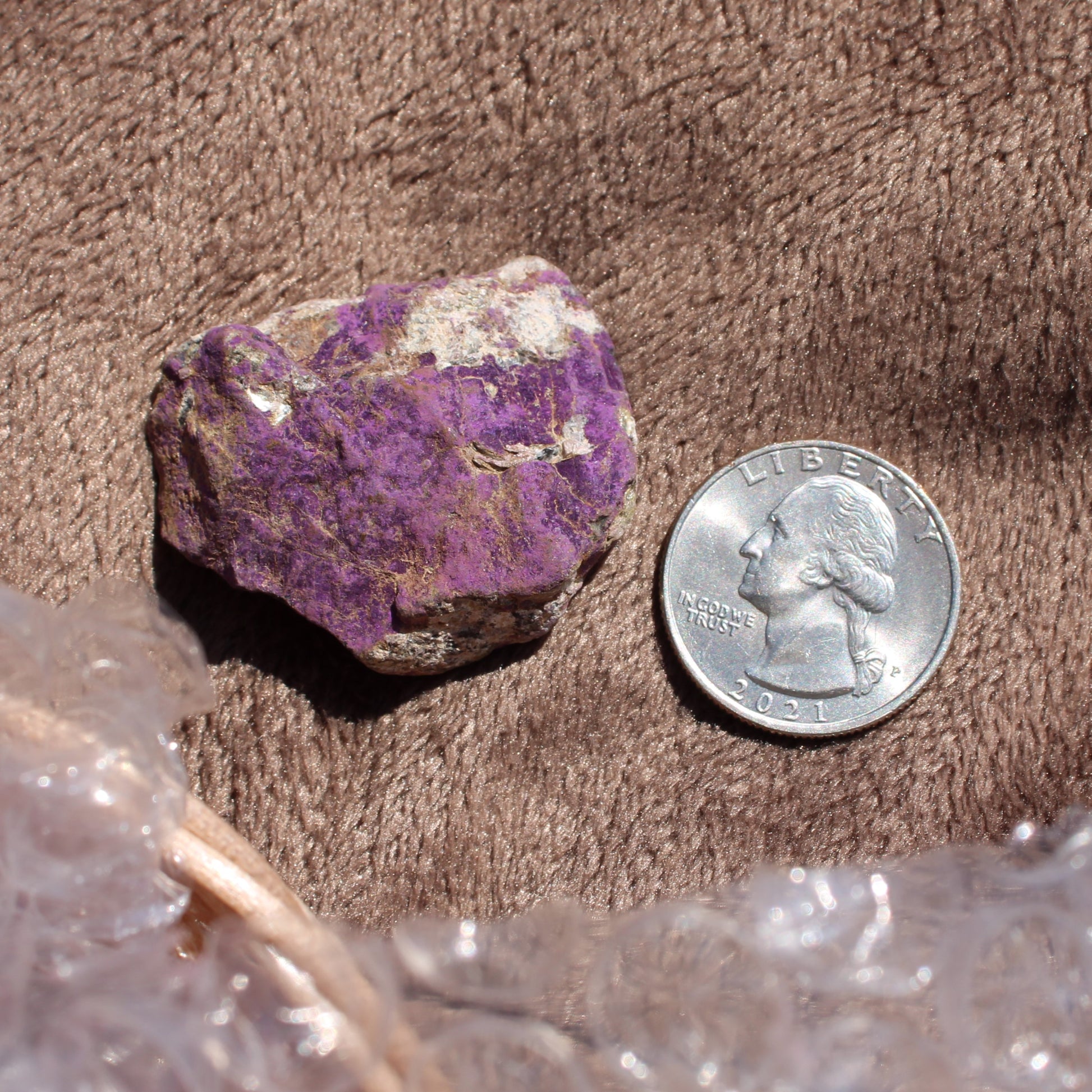 Raw Phosphosiderite crystal in purple next to a quarter for size reference