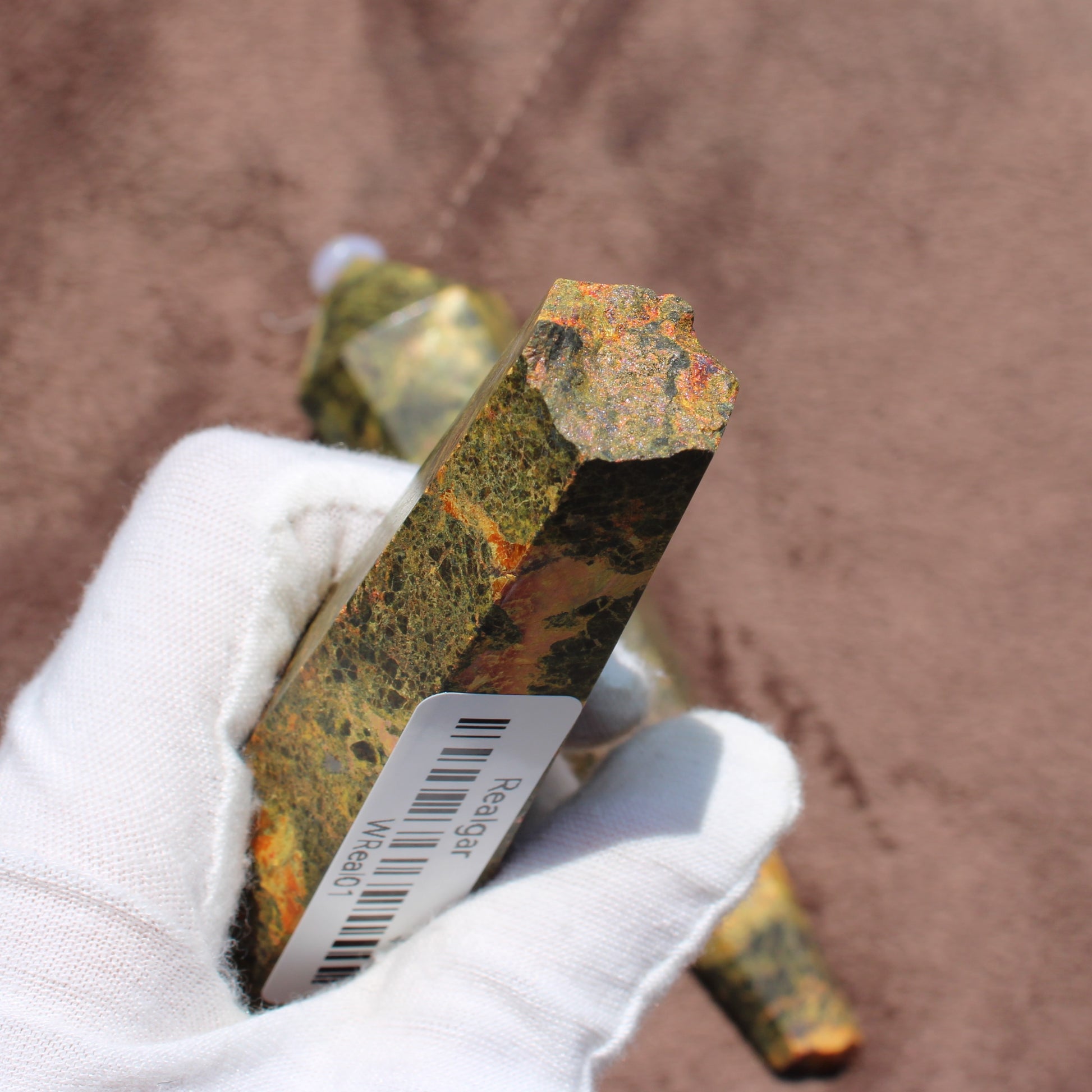 Realgar Wand crystal held in white glove by Different Branches LLC showing orange and green natural mineral textures