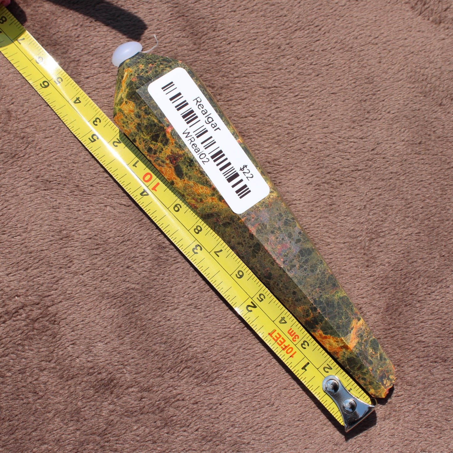 Realgar Wand crystal from Different Branches LLC measured next to a tape for size on a brown surface