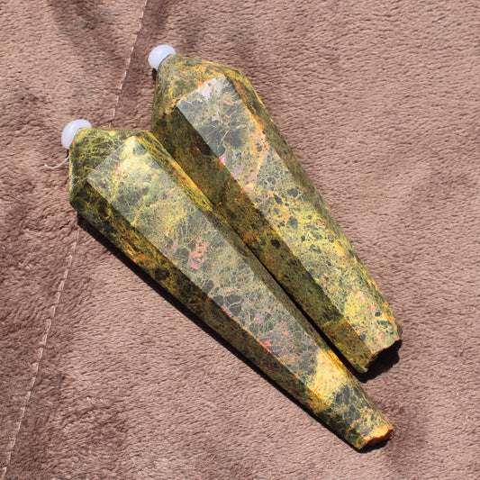 Two polished Realgar Wand crystals with golden and green hues on a brown surface