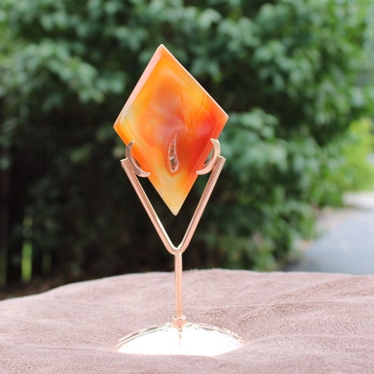Red Agate Diamond crystal on a rose gold metal stand with a blurred green outdoor background