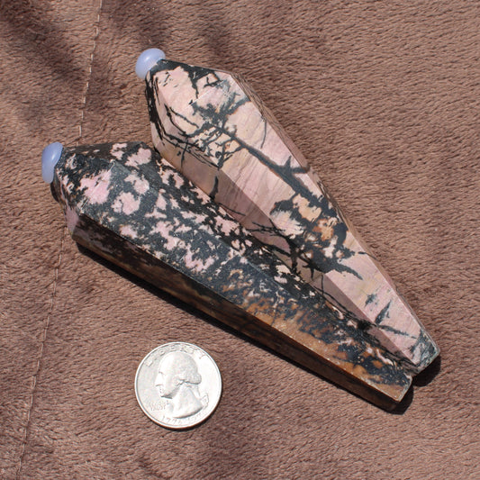 Two polished Rhodonite Wand crystals with pink and black patterns beside a quarter for size comparison