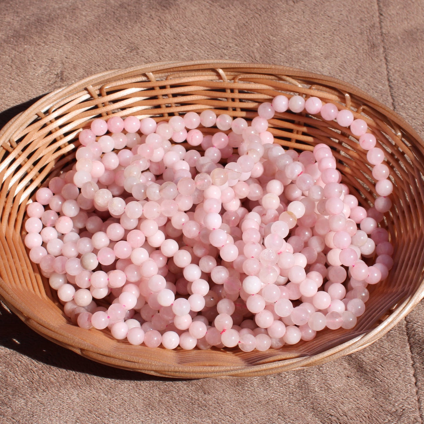 Rose Quartz Bracelet displayed in a woven basket, showcasing its soft pink tones and smooth surface