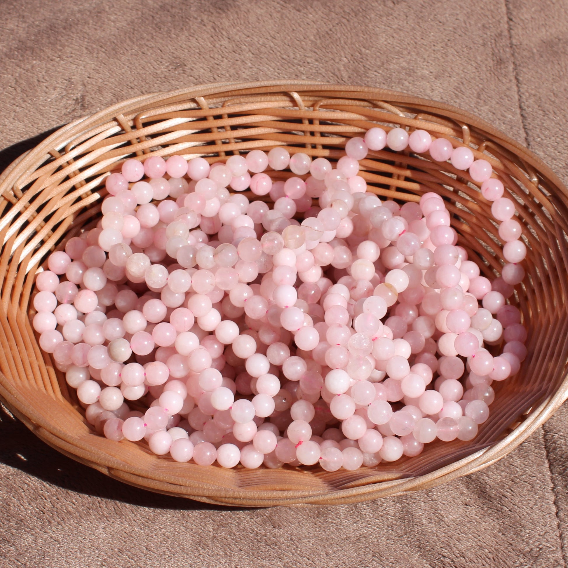 Rose Quartz Bracelet displayed in a woven basket, showcasing its soft pink tones and smooth surface