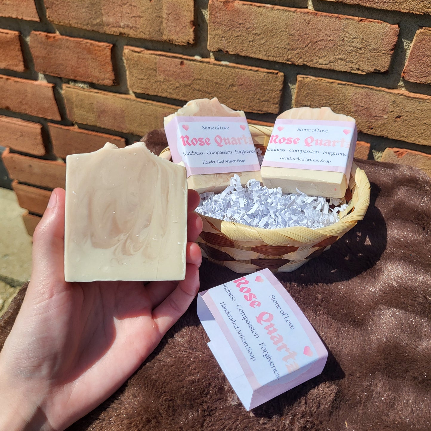 Hand holding Rose Quartz Crystal Inspired Soap Rose Geranium & Vanilla with packaging in a wicker basket