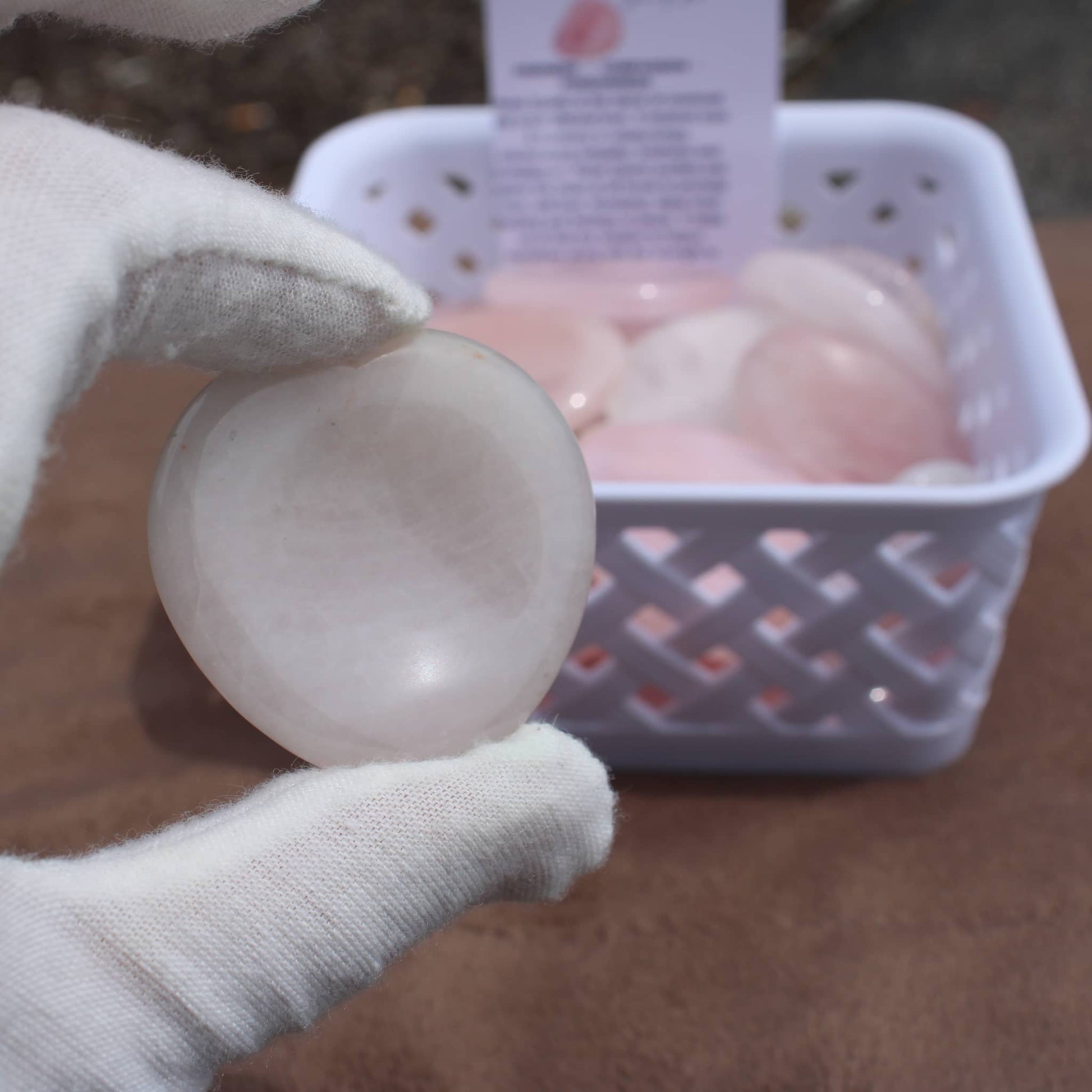 Hand holding a smooth Rose Quartz Worry Stone with basket of similar stones in the background