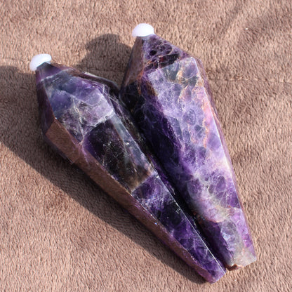 Two polished Thick Amethyst Wand crystals with deep purple hues on a textured brown surface