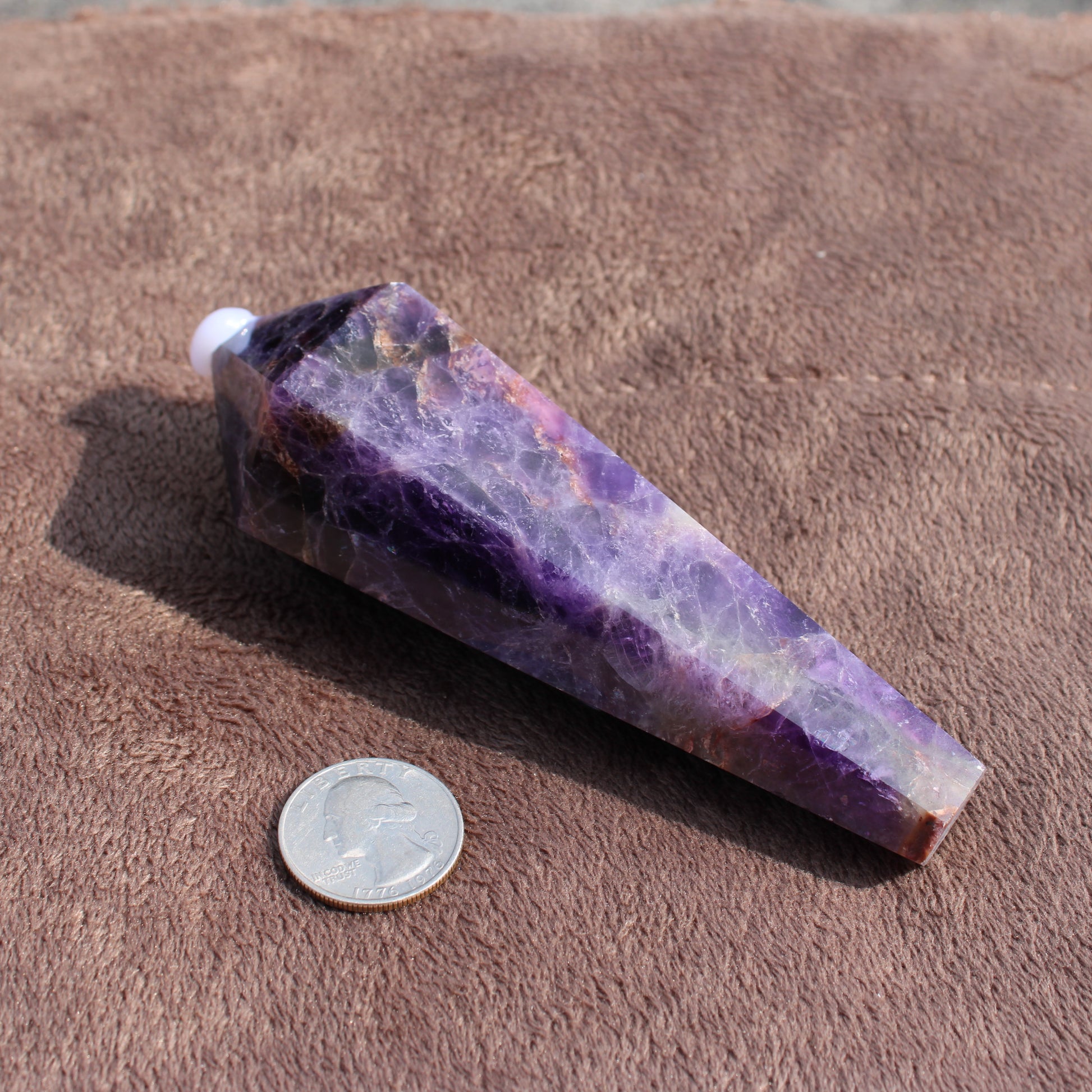Thick Amethyst Wand crystal with purple hues placed next to a quarter for size comparison