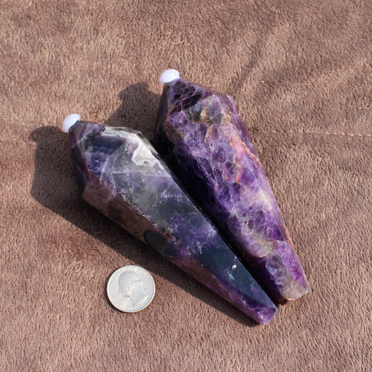 Two thick amethyst wands with deep purple hues placed next to a dime for size comparison
