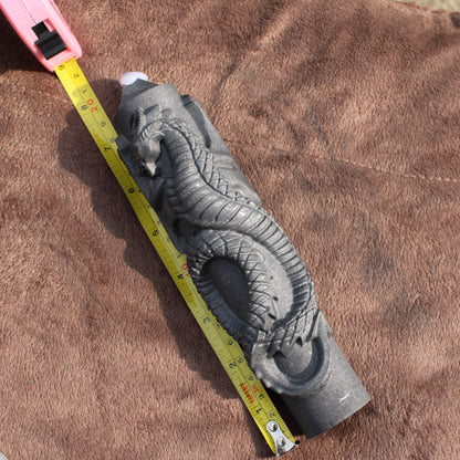 Shungite Dragon Tower crystal carved with detailed dragon design next to measuring tape on brown fabric