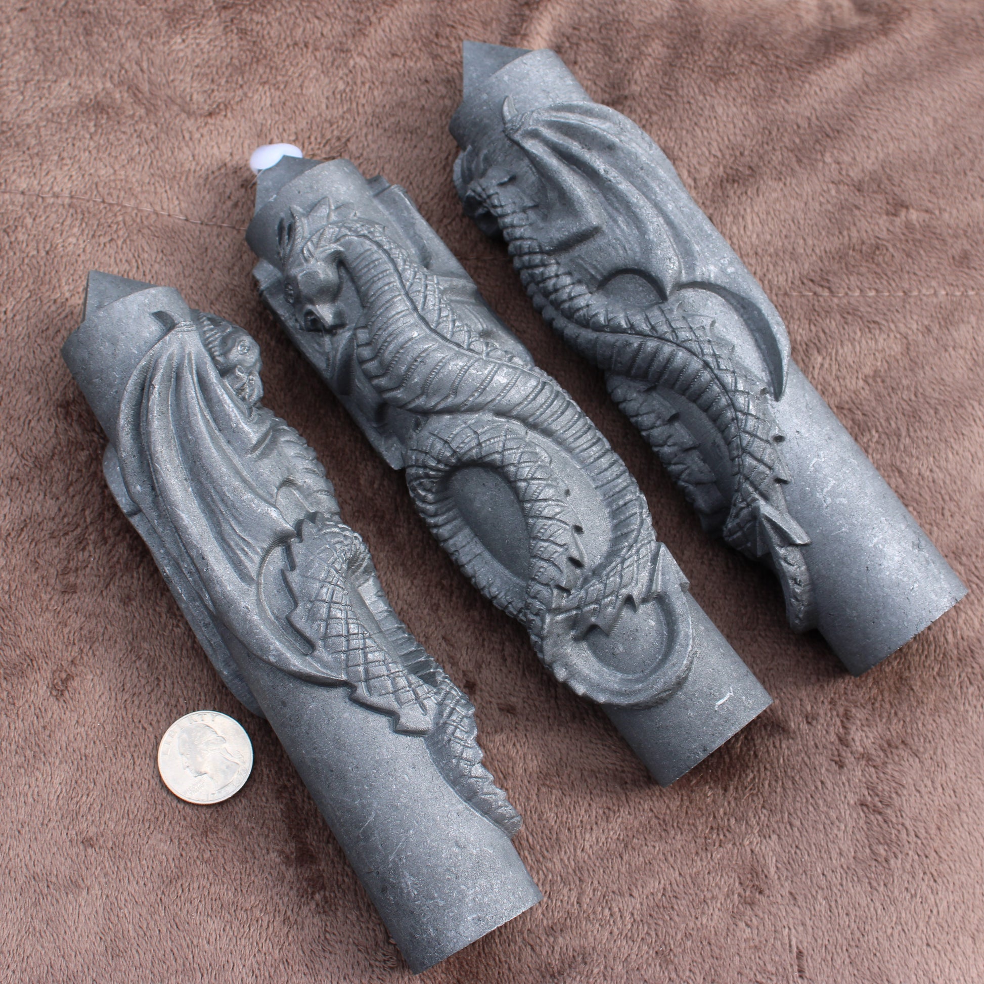 Three Shungite Dragon Tower crystal carvings displayed on a brown fabric with a coin for size reference