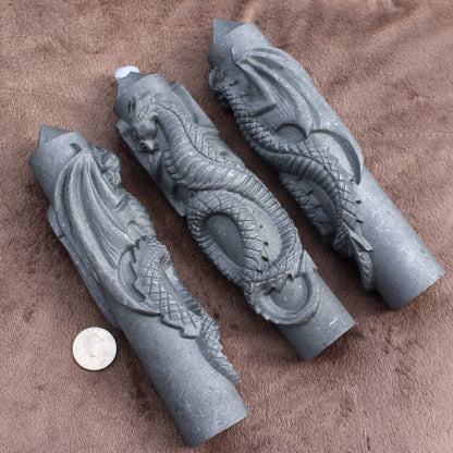 Three Shungite Dragon Tower crystal carvings displayed on a brown fabric with a coin for size reference
