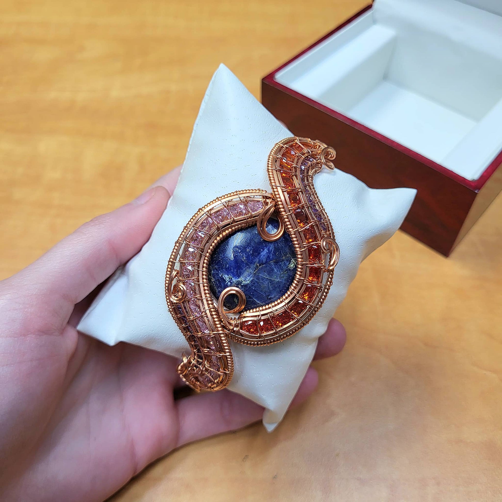 Elegant Sodalite raw copper bracelet displayed on a cushion, showcasing intricate wirework and gemstones