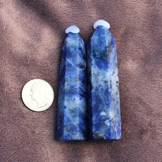 Two polished blue Sodalite Tower crystals next to a quarter for size comparison on a brown fabric background