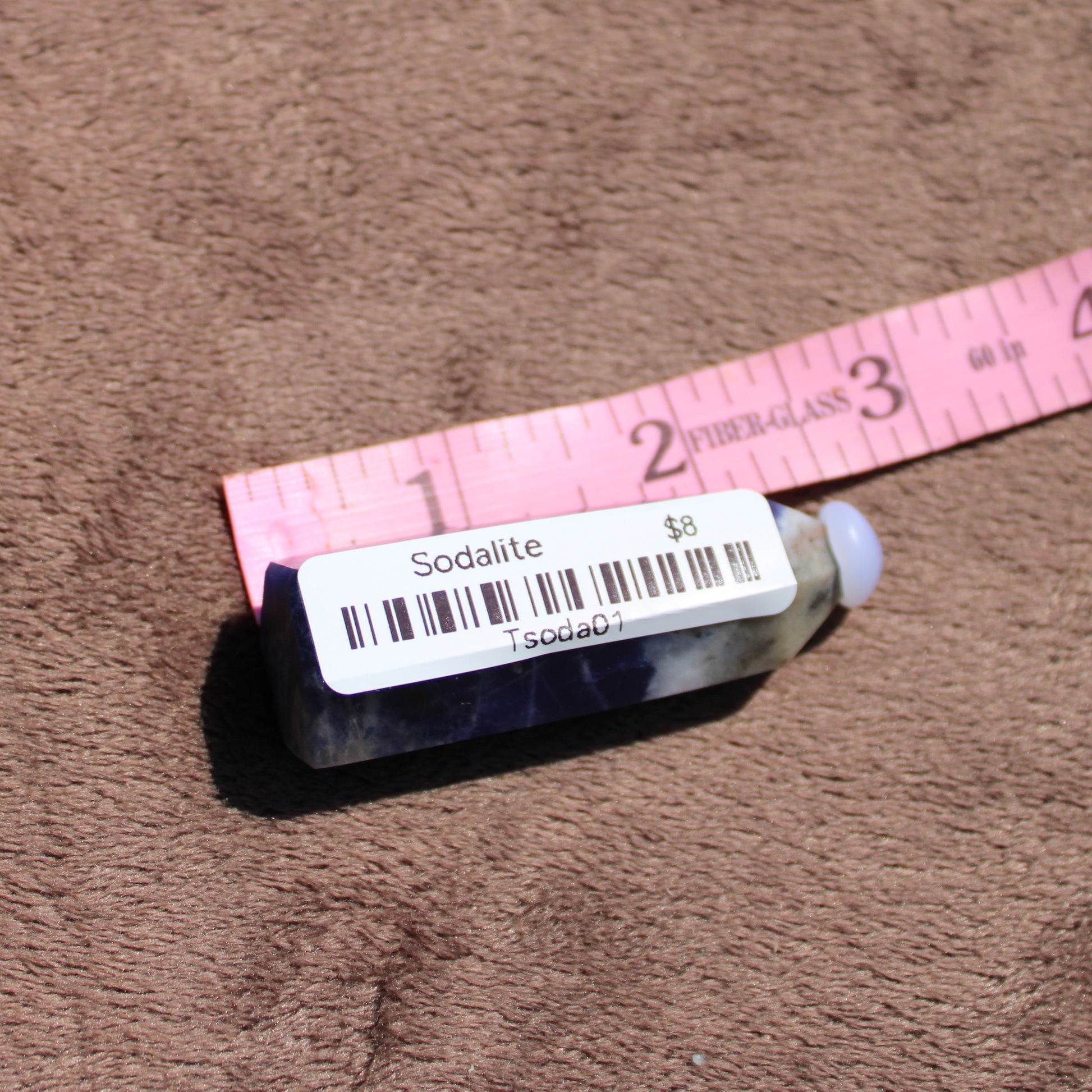 Sodalite tower with deep blue hues on a soft background next to a measuring tape for size reference