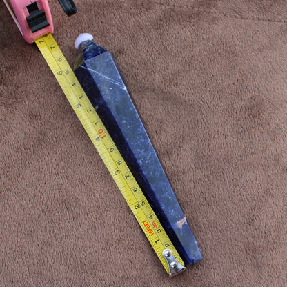 Sodalite Wand crystal with deep blue color placed next to a measuring tape on a brown fabric background