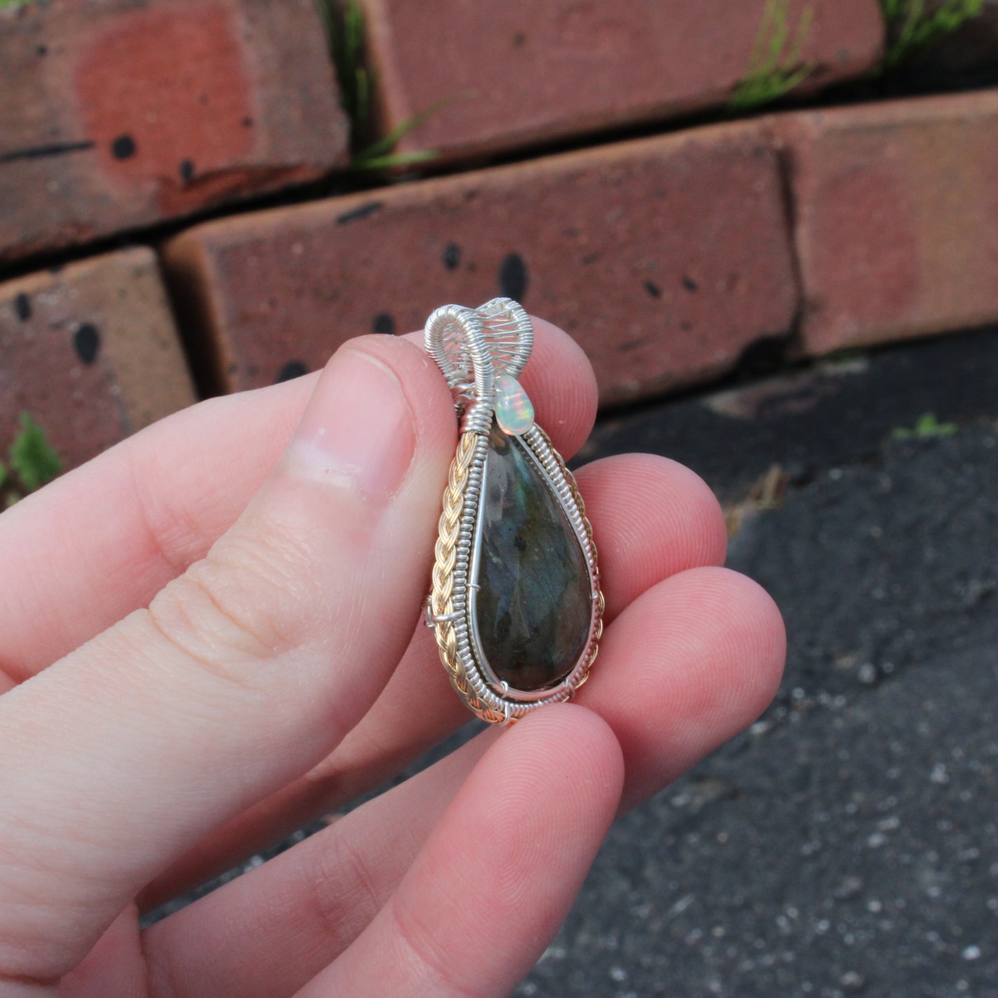 Sterling Silver Labradorite Ethiopian Opal Tear Drop Pendant held in hand against a brick background