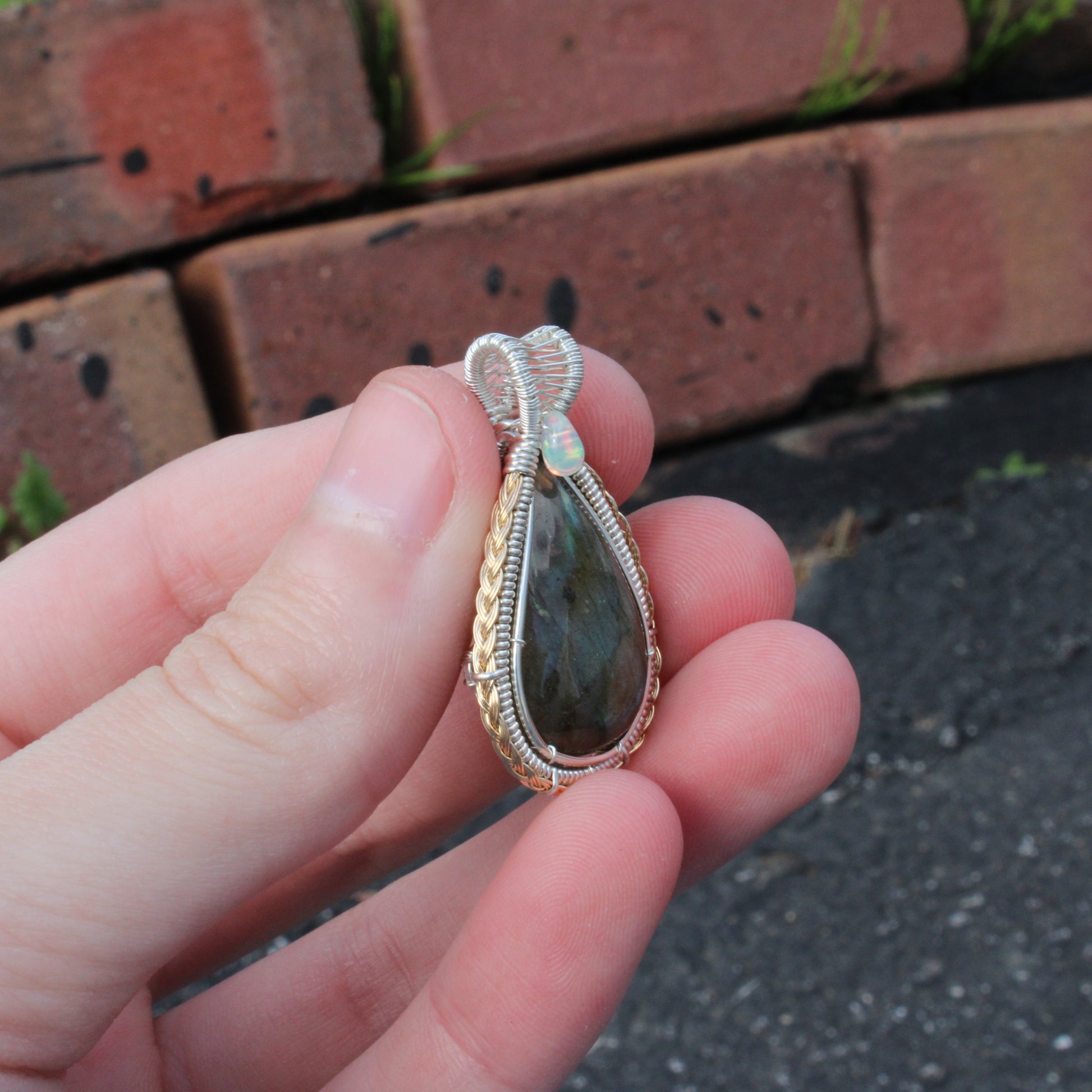Sterling Silver Labradorite Ethiopian Opal Tear Drop Pendant held in hand against a brick background